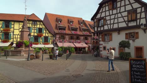 älteres-Ehepaar-Macht-Fotos-Vor-Dem-Brunnen-Im-Dorf-Ribeauvillé