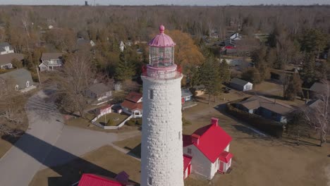 A-historic-white-lighthouse-with-a-red-roof-surrounded-by-residential-houses,-trees-in-a-serene-neighborhood,-aerial-view