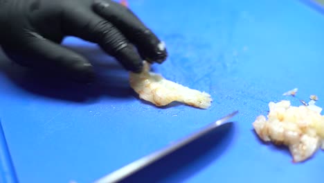 Chef-hands-cutting-shrimps-on-blue-cutting-board,-close-up