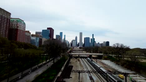 Imágenes-De-Drones-Aéreos-FPV-De-Un-Dron-Volando-Detrás-De-Un-Tren-A-Través-Del-Patio-De-Trenes-Y-Luego-Girando-180-Grados-Hacia-Un-Parque-De-La-Ciudad-Durante-El-Día,-La-Estatua-De-La-Ciudad-Se-Alza-En-La-Colina