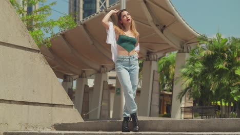 Roaming-the-streets-of-a-Caribbean-urban-center,-a-young-girl-in-jeans-and-boots-takes-in-the-sights,-with-tall-buildings-rising-in-the-distance