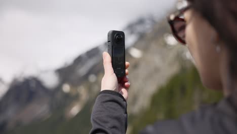 Female-traveler-takes-photo-of-mountain-scenery-with-360-degree-action-camera