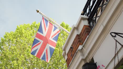 Slow-motion-Union-Jack-blows-in-the-wind-in-front-of-blossoming-tree-on-a-summer-day