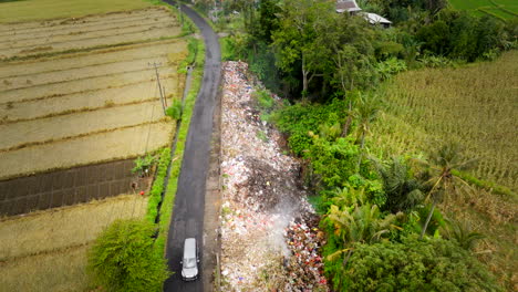 Montón-De-Basura-Humeante-Junto-A-La-Carretera-En-El-Exuberante-Paisaje-Agrícola-De-Bali,-Aéreo