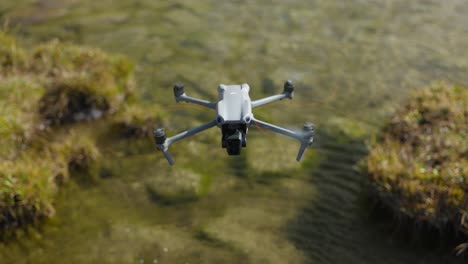DJI-Air-2S-modern-quadcopter-drone-with-green-blinking-lights-in-static-flight-over-mountain-lake-water,-close-up