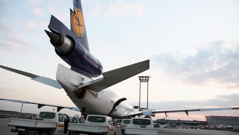 Close-up-of-Lufthansa-airplane-tail-at-airport-during-sunrise,-service-vehicles-nearby