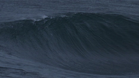 Ocean-wave-rises-with-textured-water-spraying-mist-off-top-as-it-breaks