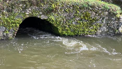 Fast-flowing-water-coming-through-a-drain-in-a-stone-bridge