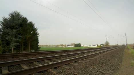 Blurred-freight-train-speeding-along-tracks-surrounded-by-greenery,-cloudy-day