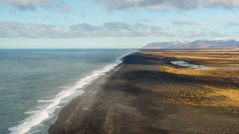 A-vast-black-sand-beach-in-iceland,-showcasing-the-striking-contrast-between-the-dark-shoreline-and-the-ocean,-aerial-view