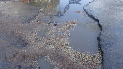 Pfützen-Und-Risse-In-Der-Straße-Aufgrund-Schlechter-Straßeninstandhaltung,-Abgenutztem-Asphalt,-Pfanne