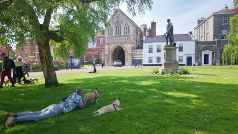 Man-with-dog-relaxes,-Norwich-Cathedral-grounds-viewing-Duke-of-Wellington-statue