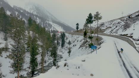 Aerial-Rising-Shot-From-Side-Of-Snow-Covered-Road-In-Naltar-Valley,-Gilgit