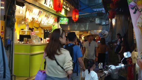 Tourists-wander-through-a-bustling-narrow-lane-flanked-by-food-stalls,-souvenir-boutiques,-and-quaint-gift-shops-in-Jiufen-Old-Street,-a-charming-mountain-village-town-in-Taiwan
