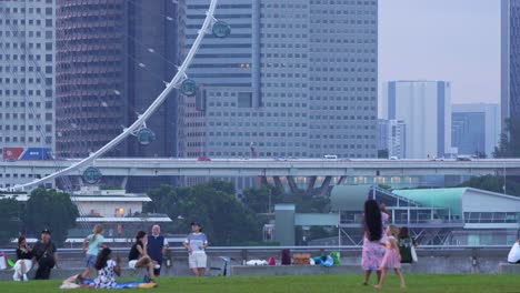 People-picnic-and-hangout-on-the-green-grass-of-Marina-barrage-rooftop-urban-park-with-Singapore-Flyer-observation-wheel-and-downtown-cityscape-in-the-background