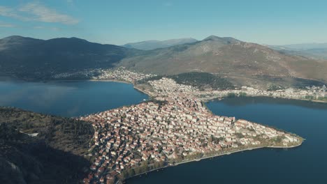 Drone-EPIC-FLIGHT-above-a-village-on-a-hill-in-Europe,-red-roof-tops,-little-houses,-sunny-weather,-blue-water-lake,-SCENIC-mountains,-Greece-4K