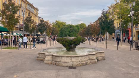 Cours-Mirabeau-street-in-Aix-en-Provence,-France,-with-fountain-and-people-on-cloudy-day