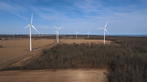 Wind-turbines-in-a-rural-setting-with-clear-skies-and-forest-backdrop,-highlighting-renewable-energy-sources,-aerial-view