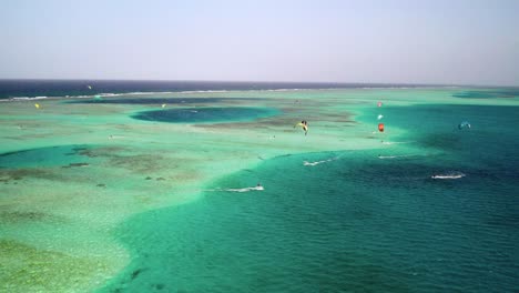 Kitesurfers-gliding-over-a-vibrant-coral-reef-on-a-sunny-day,-aerial-view