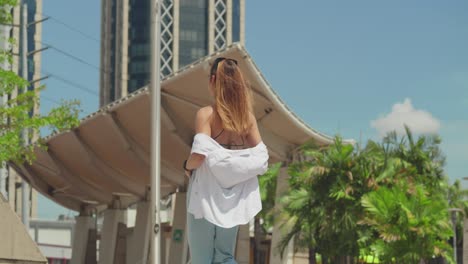 Amidst-the-hustle-of-a-Caribbean-city,-a-girl-in-jeans-and-boots-explores,-with-tall-buildings-providing-a-dramatic-backdrop