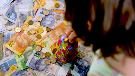 Child-saves-South-African-coins-into-money-box,-telephoto-over-shoulder-shot