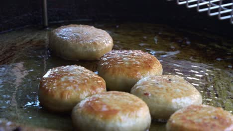 The-food-stall-vendor-uses-kitchen-tongs-to-flip-the-meat-pies-sizzling-in-the-hot-oil-pan,-pan-frying-them-until-golden-brown,-close-up-shot-of-popular-Asian-food