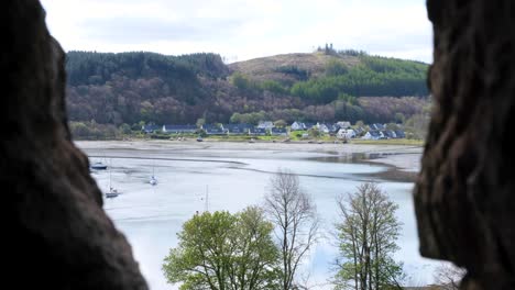 View-through-the-archers-window-of-historical-Dunstaffnage-Castle-overlooking-ocean-water-and-houses-in-Oban,-Argyll-and-Bute,-Western-Scotland-UK