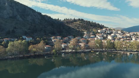 Drone-orbit-FLIGHT-aside-to-a-village-on-a-hill-in-Europe,-red-roof-tops,-sunny-weather,-blue-water-lake,-SCENIC-mountains,-Greece-4K-dreamy-video