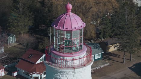 Ein-Malerischer-Leuchtturm-Mit-Einer-Auffallenden-Rosa-Spitze,-Eingebettet-In-üppiges-Grün-An-Einem-Sonnigen-Tag,-Luftaufnahme