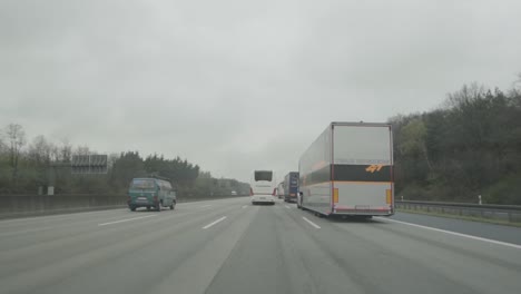 POV-De-Coche-Rodado-En-Una-Carretera-Muy-Transitada-Con-Furgonetas-Y-Camiones-Bajo-Un-Cielo-Nublado