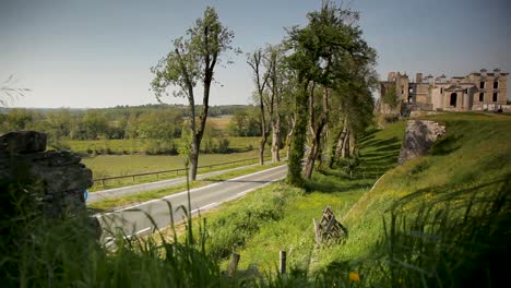 Scenic-view-of-an-ancient-castle-beside-a-curvy-road-with-lush-greenery-on-a-sunny-day