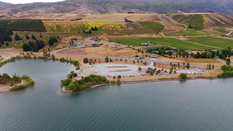 Aerial-view-of-Lake-Dunstan-next-to-Lowburn-in-Cromwell,-showing-serene-blue-waters-bordered-by-golden-hued-hills-and-a-recreational-area