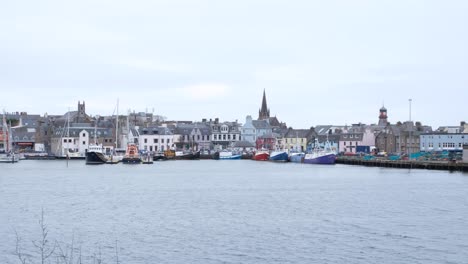 Slow-pan-of-Stornoway-town-and-harbour-with-traffic,-houses,-shops,-and-moored-ships-and-boat-in-Outer-Hebrides-of-Scotland-UK