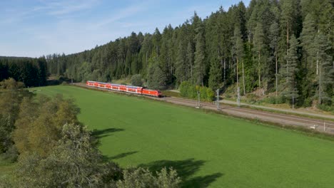 A-bright-red-deutsche-bahn-train-speeding-through-a-lush-green-landscape,-aerial-view