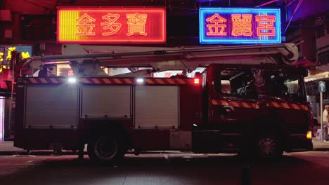 Fire-truck-by-blinking-neon-lights-at-night-in-Hong-Kong,-street-view