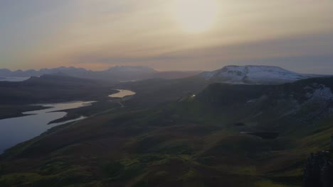 Slow-dolly-out-aerial-reveals-lush-green-Scottish-highlands-contrasting-with-the-snow-covered-cliffs-of-the-Isle-of-Skye,-Scotland