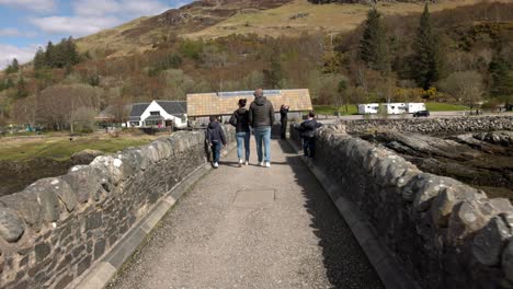 POV-Aufnahme-Einer-Familie,-Die-Entlang-Der-Eilean-Donan-Bridge-Spaziert-Und-Die-Sehenswürdigkeiten-Erkundet