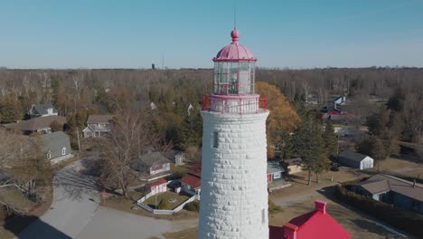 A-historic-white-lighthouse-with-a-red-top-in-a-residential-area,-bright-daylight,-aerial-view