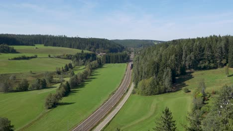 A-train-passing-through-lush-green-countryside-with-forested-hills,-aerial-view