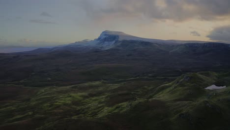 Un-Vuelo-Tranquilo-Sobre-Verdes-Tierras-Altas-Domina-Una-Montaña-Cubierta-De-Nieve-En-El-Paseo-Quiraing,-Isla-De-Skye,-Escocia