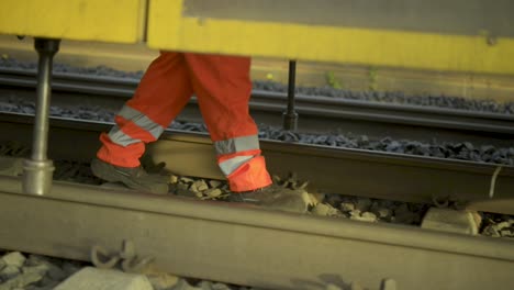 Un-Trabajador-Ferroviario-Con-Ropa-De-Alta-Visibilidad-Inspecciona-Las-Vías-Al-Atardecer,-En-Primer-Plano