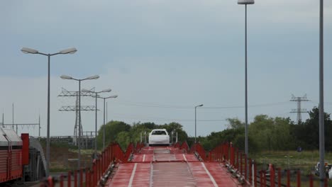 New-cars-crossing-bright-red-bridge-over-railway-tracks,-light-posts-and-electrical-lines-in-background,-daytime-shot