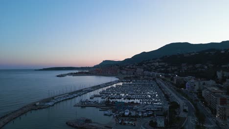 Aerial-sunset-view-of-Menton-on-the-French-Riviera,-showcasing-the-marina-and-coastal-town-layout
