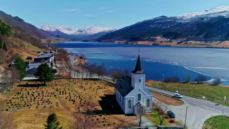 Aerial-View,-Catholic-Church,-Coastal-Road-and-Frozen-Fjord-in-Landscape-of-Norway-on-Sunny-Day,-Drone-Shot