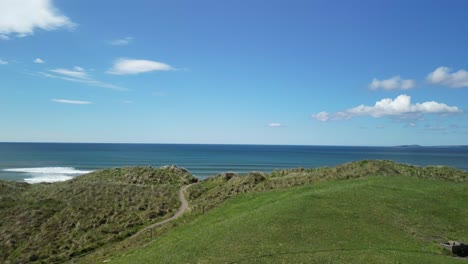 Aerial-lift-off-on-a-green-grassy-dunes-revealing-Long-Strand-beach-and-gentle-waves-of-the-Atlantic-on-a-sunny-day