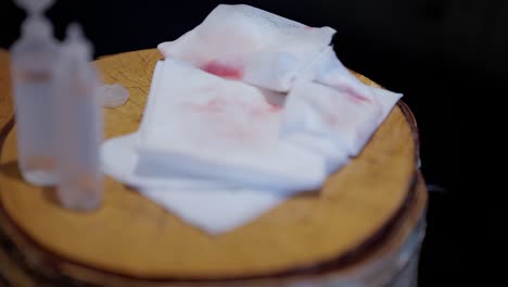 Medical-wipes-with-blood-laid-at-wooden-table-after-cleaning-wound,-shallow-depth-close-up-with-blurred-foreground