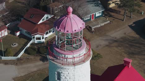 Un-Encantador-Faro-Con-Una-Cúpula-Rosa-En-Un-Día-Soleado,-Rodeado-De-Pequeños-Edificios,-Vista-Aérea