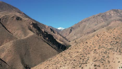 Drone-footage-of-a-remote-mountainscape-with-brown-foothills-and-snow-capped-mountain-in-the-Frank-Church-River-of-No-Return-Wilderness-in-Idaho