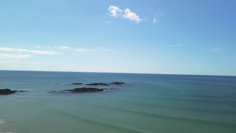 An-aerial-drone-footage-turn-over-blue-ocean-and-sunny-sky,-to-sandy-beach-and-coastal-West-Cork,-Ireland