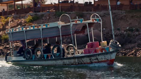 Tourist-cruise-boat-tour-on-the-coast-of-Philae-island-during-golden-hour,-slow-motion-stabilized-shot